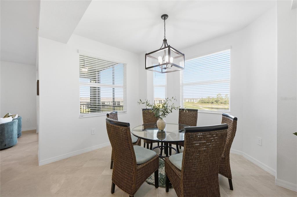 A dining area features a glass-topped table, wicker chairs, and a chandelier near windows — 17595 OPAL SAND DRIVE UNIT 302, VENICE, FL