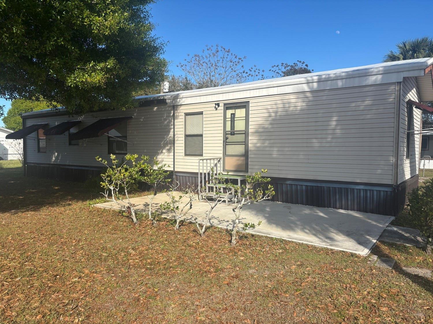Exterior view of a beige mobile home with a concrete patio and metal awnings — 4968 Amy Lane, Fort Pierce FL 34946, FORT PIERCE, FL