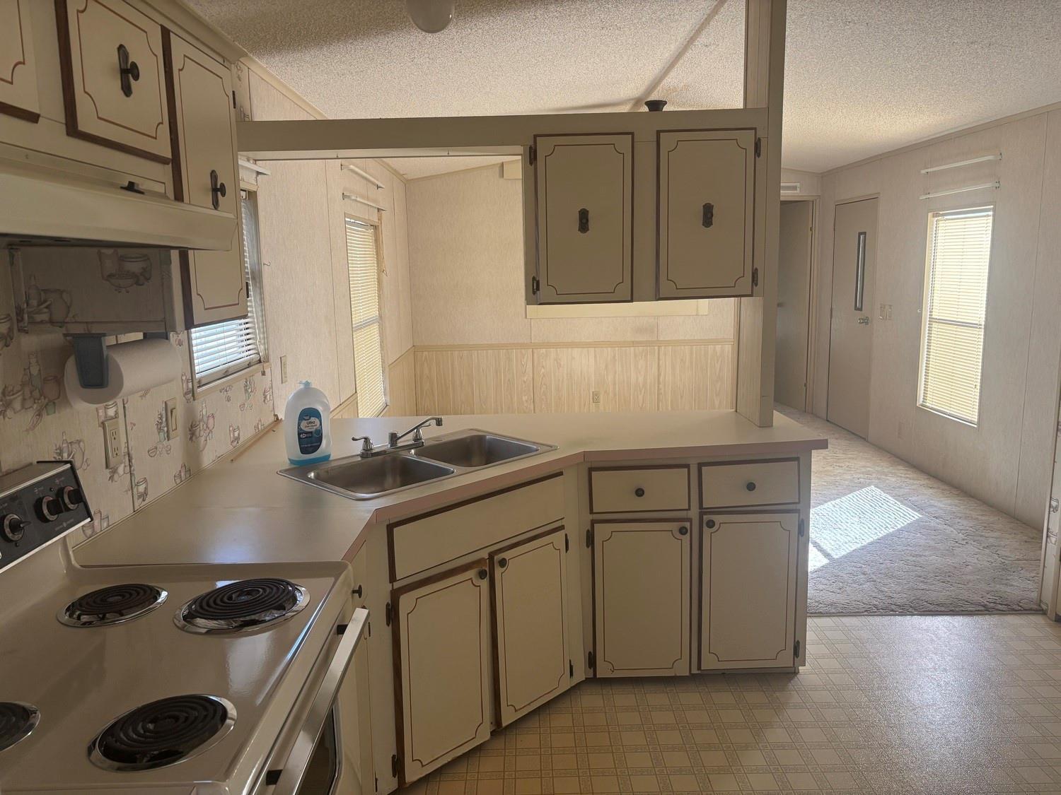 A kitchen with light-colored cabinets, a corner sink, and a stove, opening into a living area — 4968 Amy Lane, Fort Pierce FL 34946, FORT PIERCE, FL