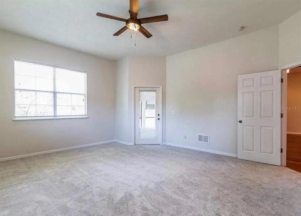 An empty bedroom with gray carpet, a ceiling fan, a window, and a glass door — 7962 SW 85TH TERRACE, GAINESVILLE, FL