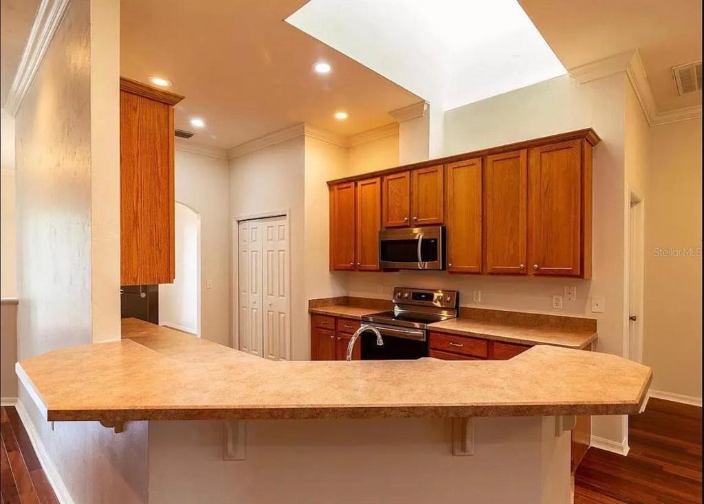 A kitchen features wood cabinets, laminate countertops, a stainless steel microwave, and a breakfast bar — 7962 SW 85TH TERRACE, GAINESVILLE, FL