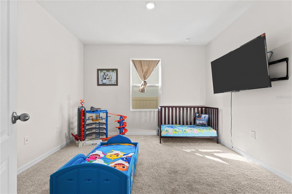 A child's bedroom features a blue toddler bed, a dark wood crib, and a wall-mounted television — 547 TANARO LANE, HAINES CITY, FL