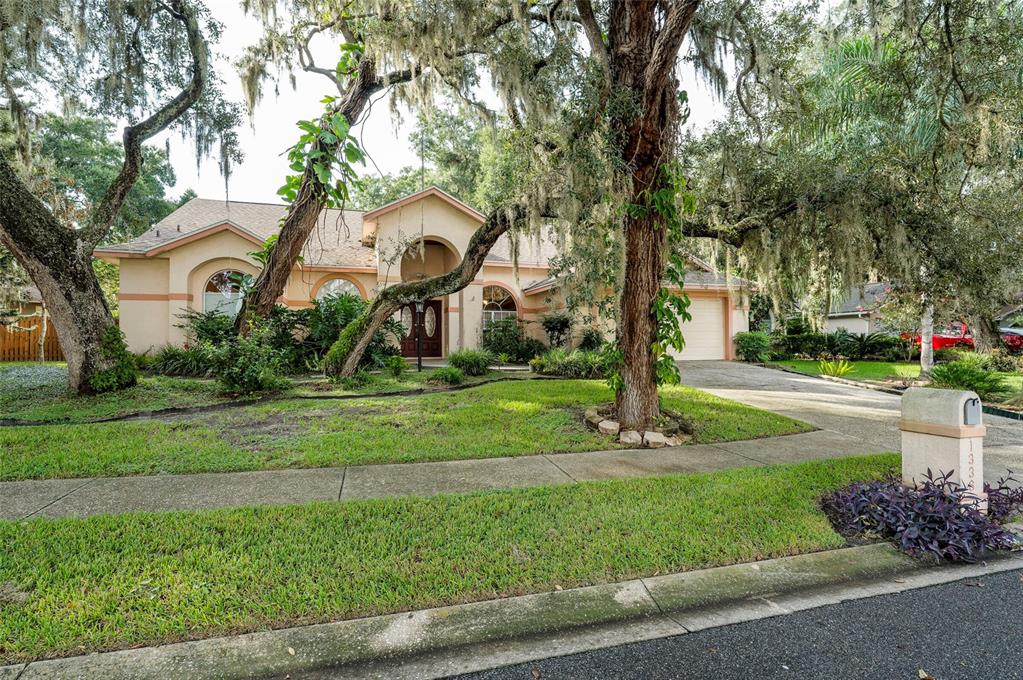 A single-story house with a beige stucco exterior, arched windows, and large oak trees — 1336 WATERWOOD DRIVE, LUTZ, FL