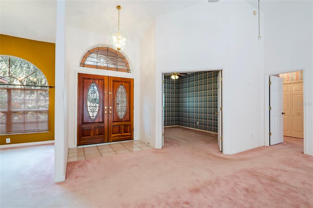An entryway with pink carpet, double wood front doors, and an adjacent room with wallpaper — 1336 WATERWOOD DRIVE, LUTZ, FL