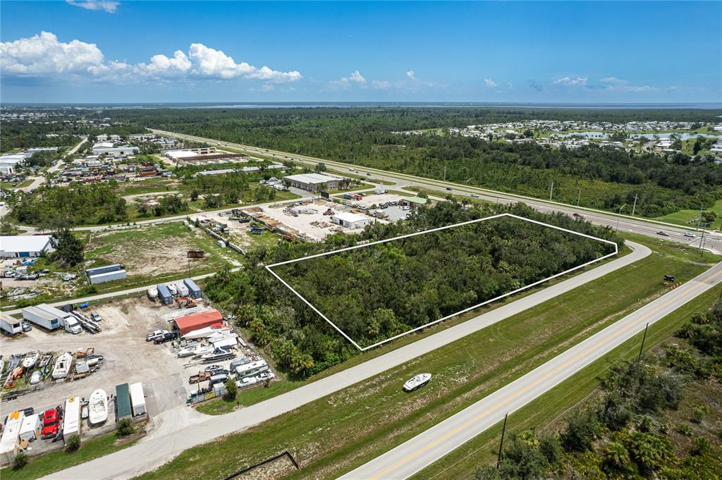 An aerial view shows a rectangular, wooded vacant lot bordered by a road and businesses — 13440 MARATHON BOULEVARD, PORT CHARLOTTE, FL