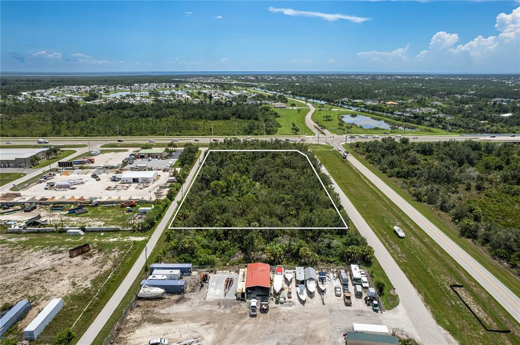 An aerial view shows a rectangular, wooded vacant lot bordered by roads and industrial properties — 13440 MARATHON BOULEVARD, PORT CHARLOTTE, FL