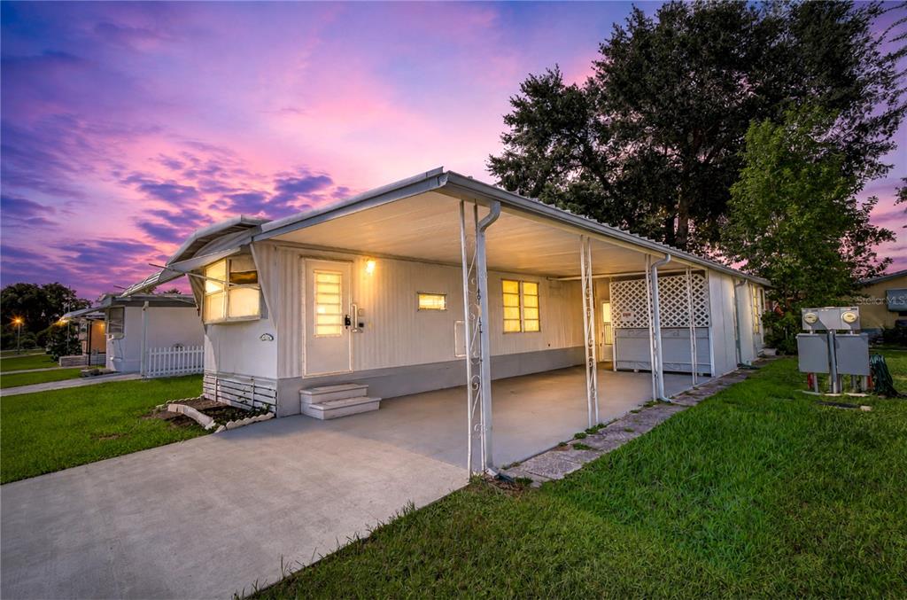 A single-story mobile home with a carport and a white exterior under a sunset sky — 38651 WINDFLOWER AVENUE, ZEPHYRHILLS, FL