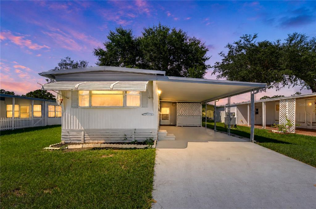 A single-story mobile home features a white exterior, a metal carport, and a concrete driveway — 38651 WINDFLOWER AVENUE, ZEPHYRHILLS, FL