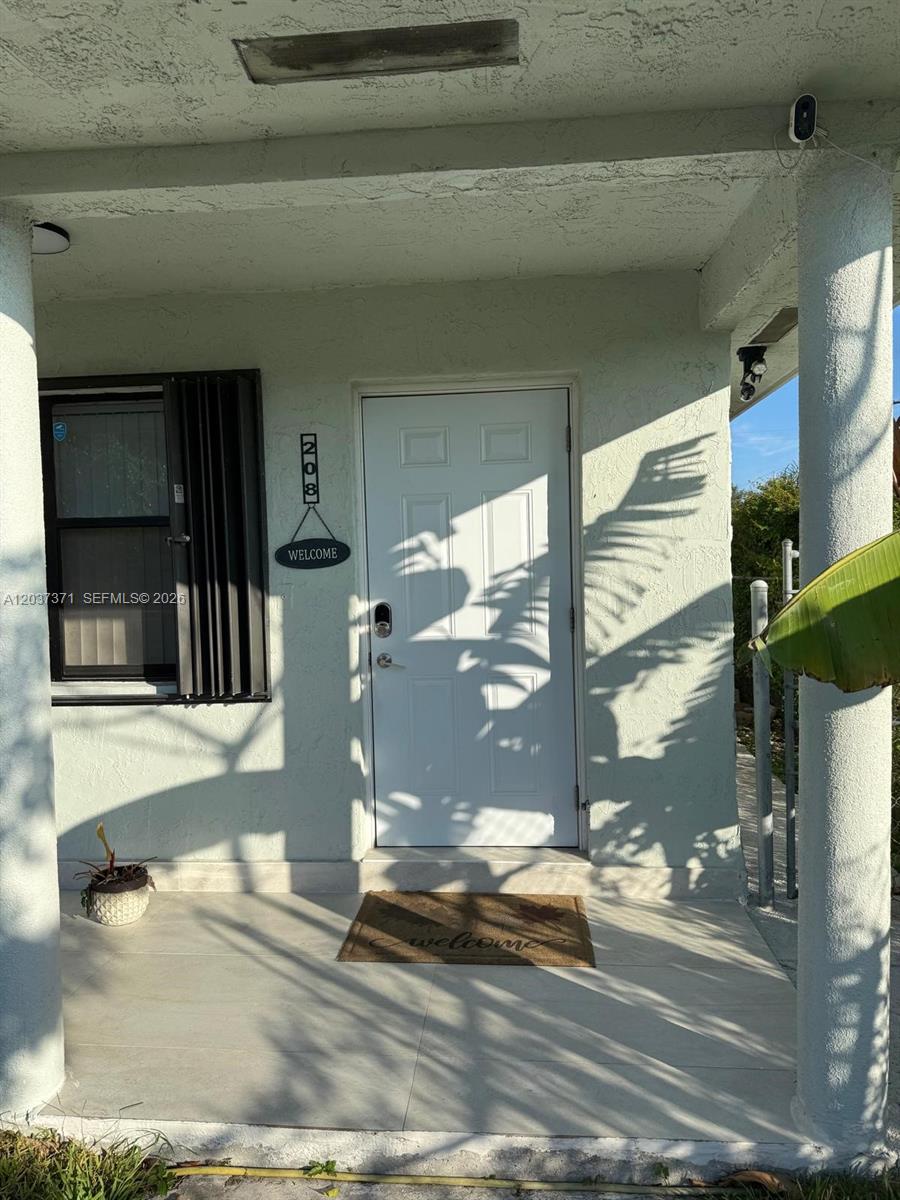 A white front door with a welcome sign and house number sits on a porch — 208 NW 7th St # 1, Hallandale Beach FL 33009, HALLANDALE BEACH, FL
