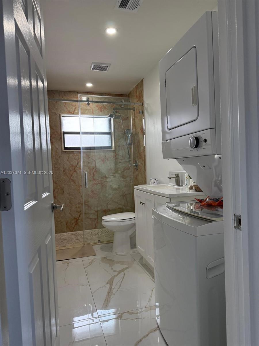 A bathroom features a stacked washer-dryer, a marble-tiled shower, and white floor tiles — 208 NW 7th St # 1, Hallandale Beach FL 33009, HALLANDALE BEACH, FL