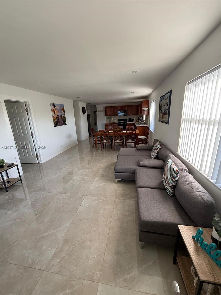 An open-concept living and dining area features light tile flooring and a gray sectional sofa — 208 NW 7th St # 1, Hallandale Beach FL 33009, HALLANDALE BEACH, FL