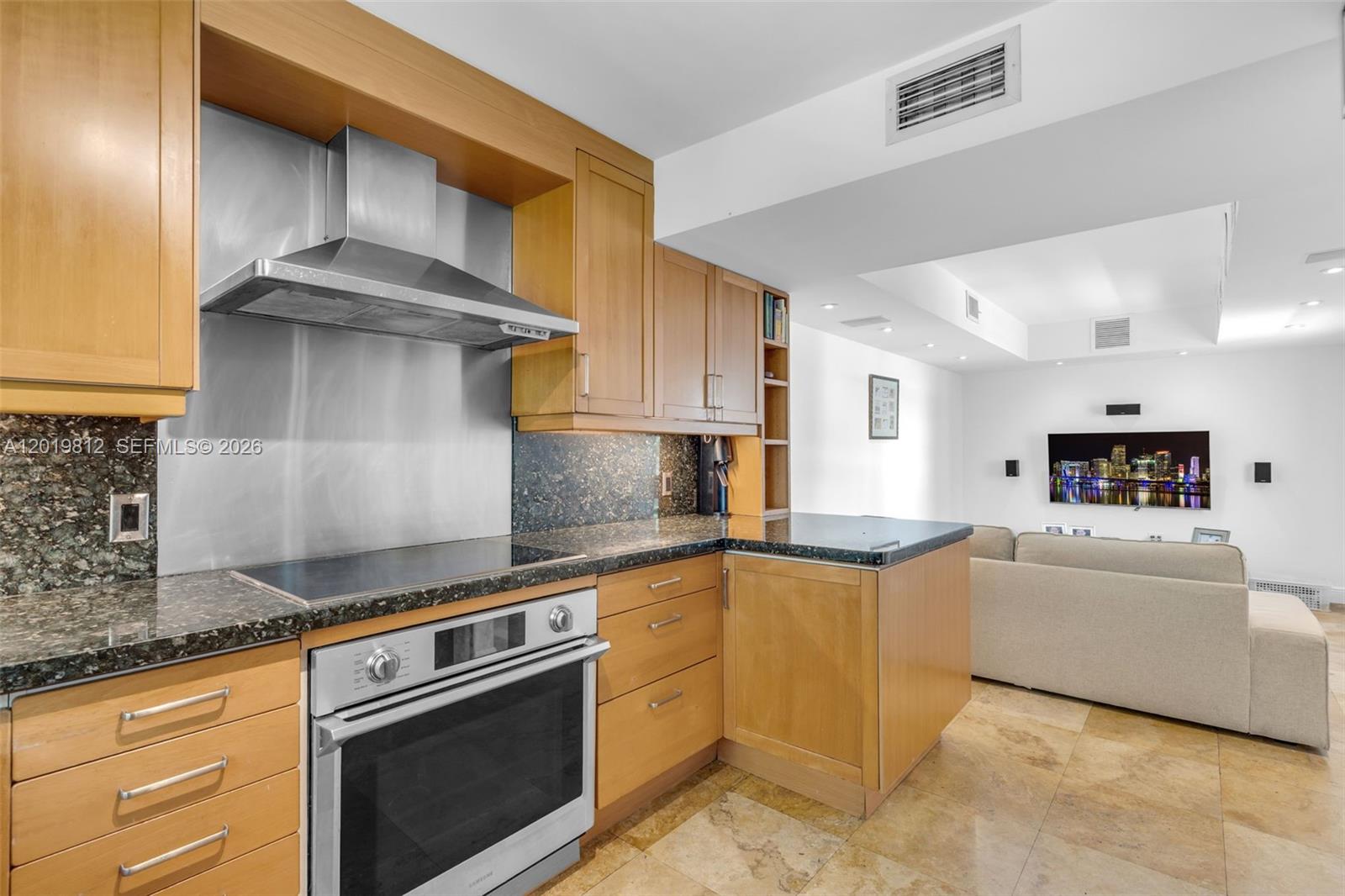A kitchen with light wood cabinets, granite countertops, and stainless steel appliances opens to a living room — 209 E Enid Dr # 36, Key Biscayne FL 33149, KEY BISCAYNE, FL