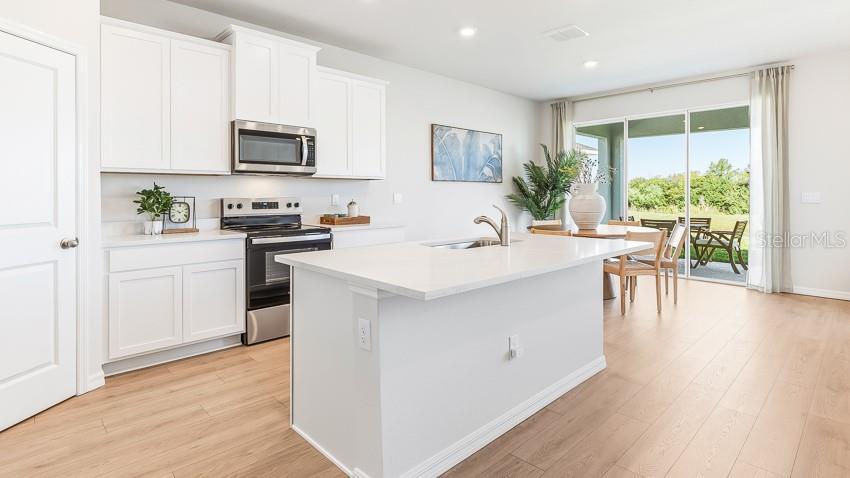 A modern kitchen features white cabinets, a central island, and sliding doors leading to a patio — 18217 GANDER TERRACE, LAKEWOOD RANCH, FL