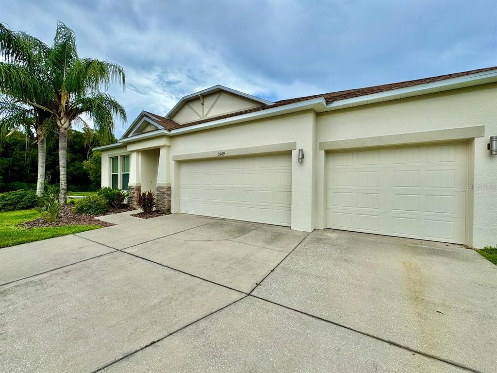A beige house exterior features a three-car garage and a concrete driveway — 3989 WINDCREST DRIVE, WESLEY CHAPEL, FL