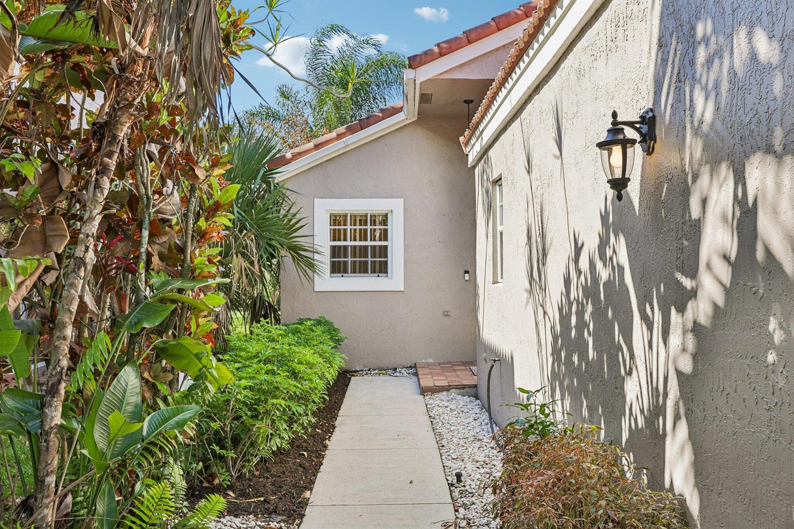 A concrete walkway leads along the side of a beige stucco house with a tiled roof — 1110 NW 105th Way, Plantation FL 33322, PLANTATION, FL