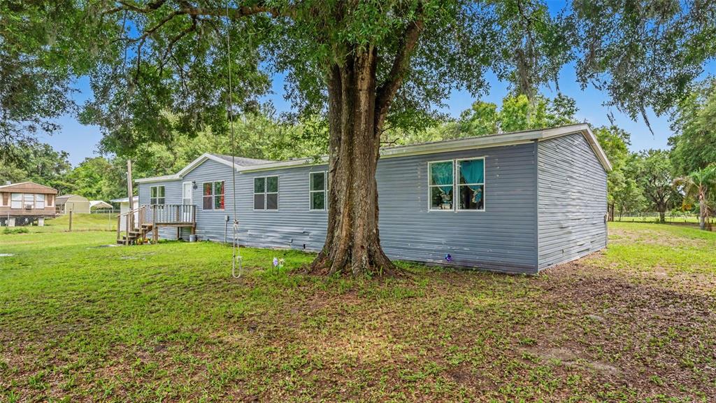 A gray manufactured home sits on a grassy lot beneath a large oak tree — 4736 WALNUT CIRCLE S, LAKELAND, FL