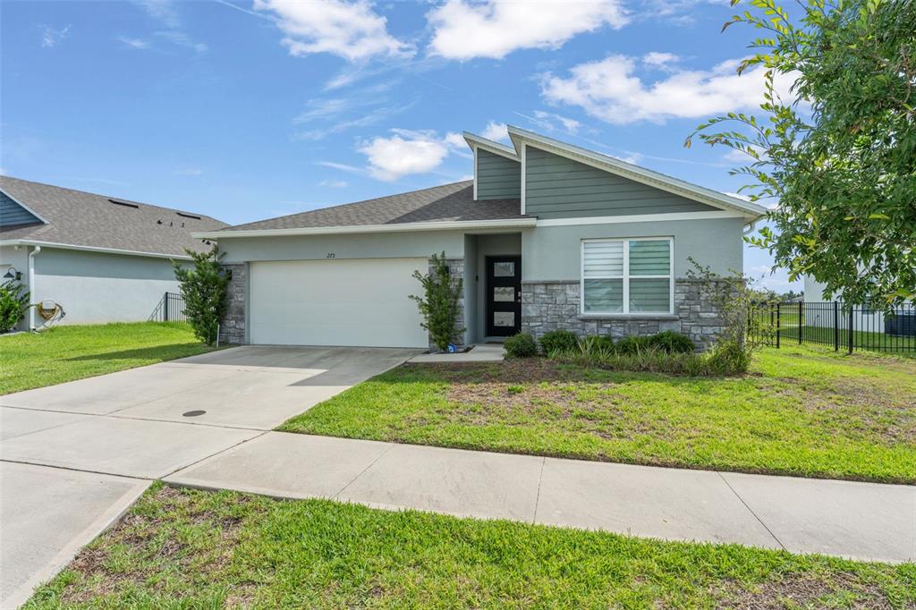 A single-story house features a two-car garage, stone veneer accents, and a modern front door — 273 TALISI LOOP, ST CLOUD, FL