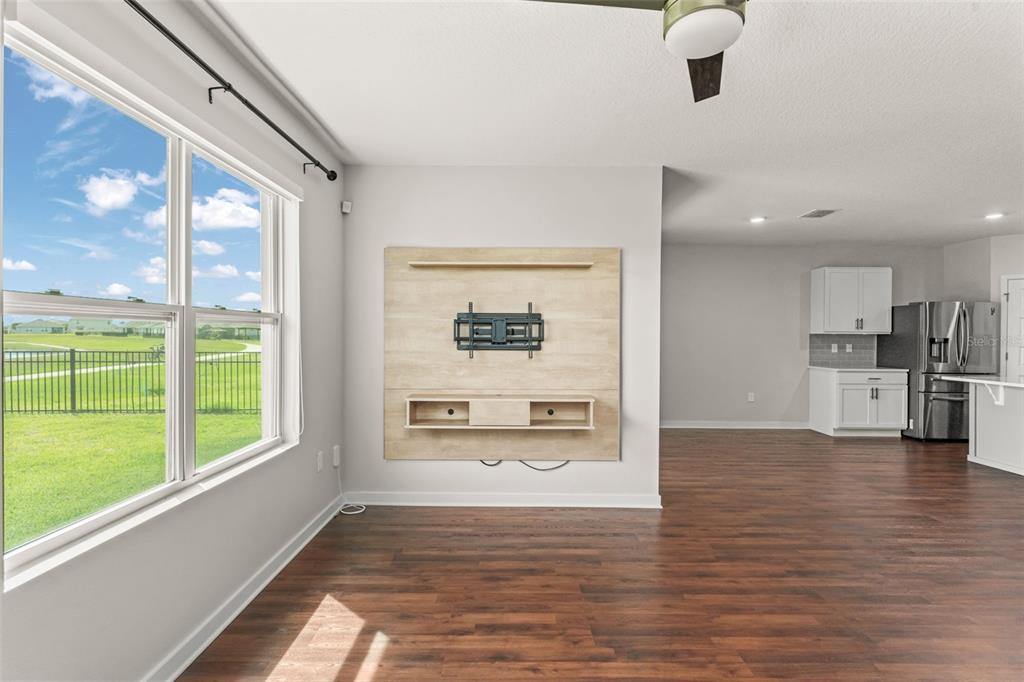 A living room with wood-look flooring, a wall-mounted media console, and a view of a yard — 273 TALISI LOOP, ST CLOUD, FL