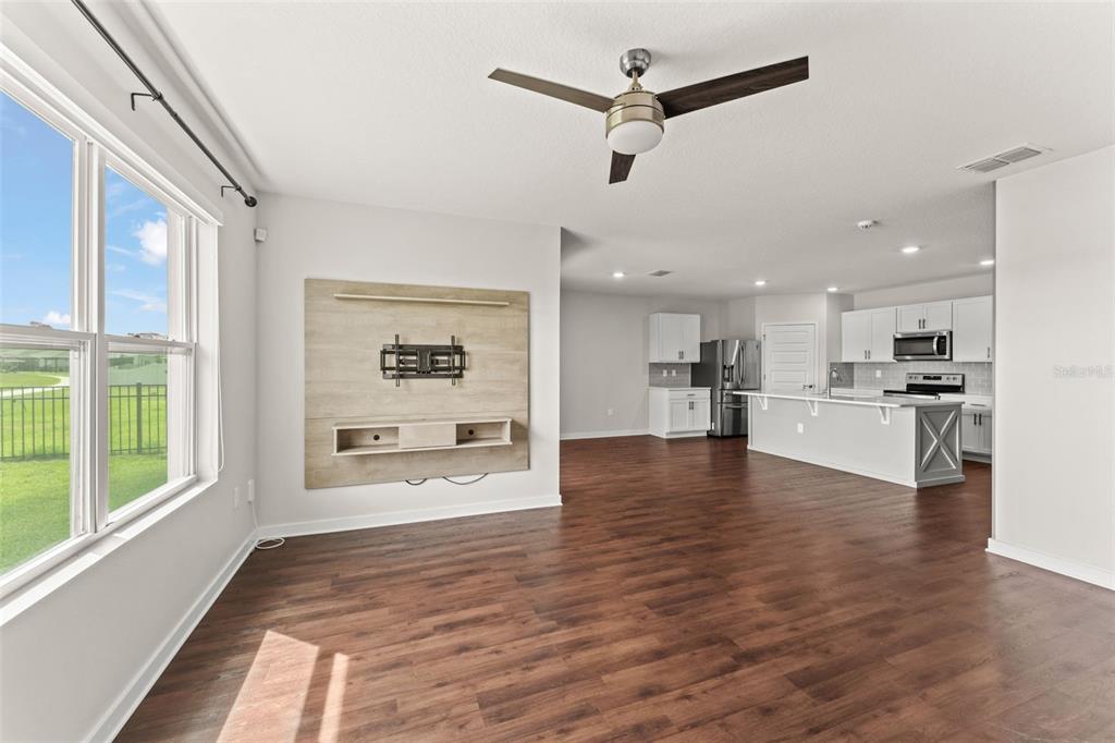 An open-concept living room and kitchen featuring wood-look flooring, a ceiling fan, and white cabinetry — 273 TALISI LOOP, ST CLOUD, FL