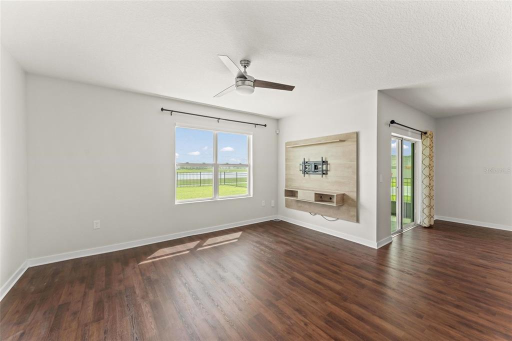 A living room with wood-look flooring, a ceiling fan, a wall-mounted media console, and windows — 273 TALISI LOOP, ST CLOUD, FL