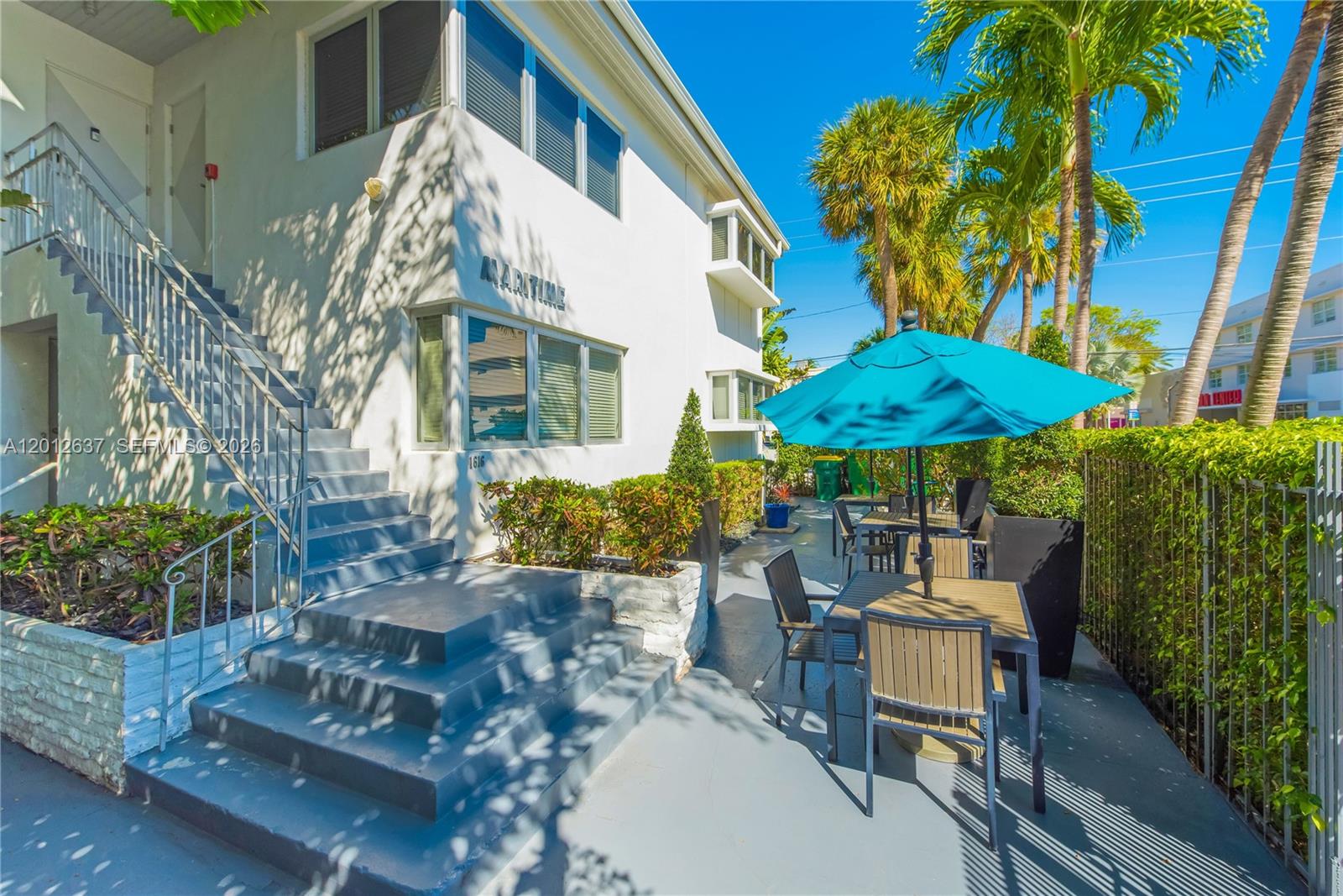 An exterior view of a white building with outdoor patio seating and a blue umbrella — 1616 Euclid Ave # 7, Miami Beach FL 33139, MIAMI BEACH, FL
