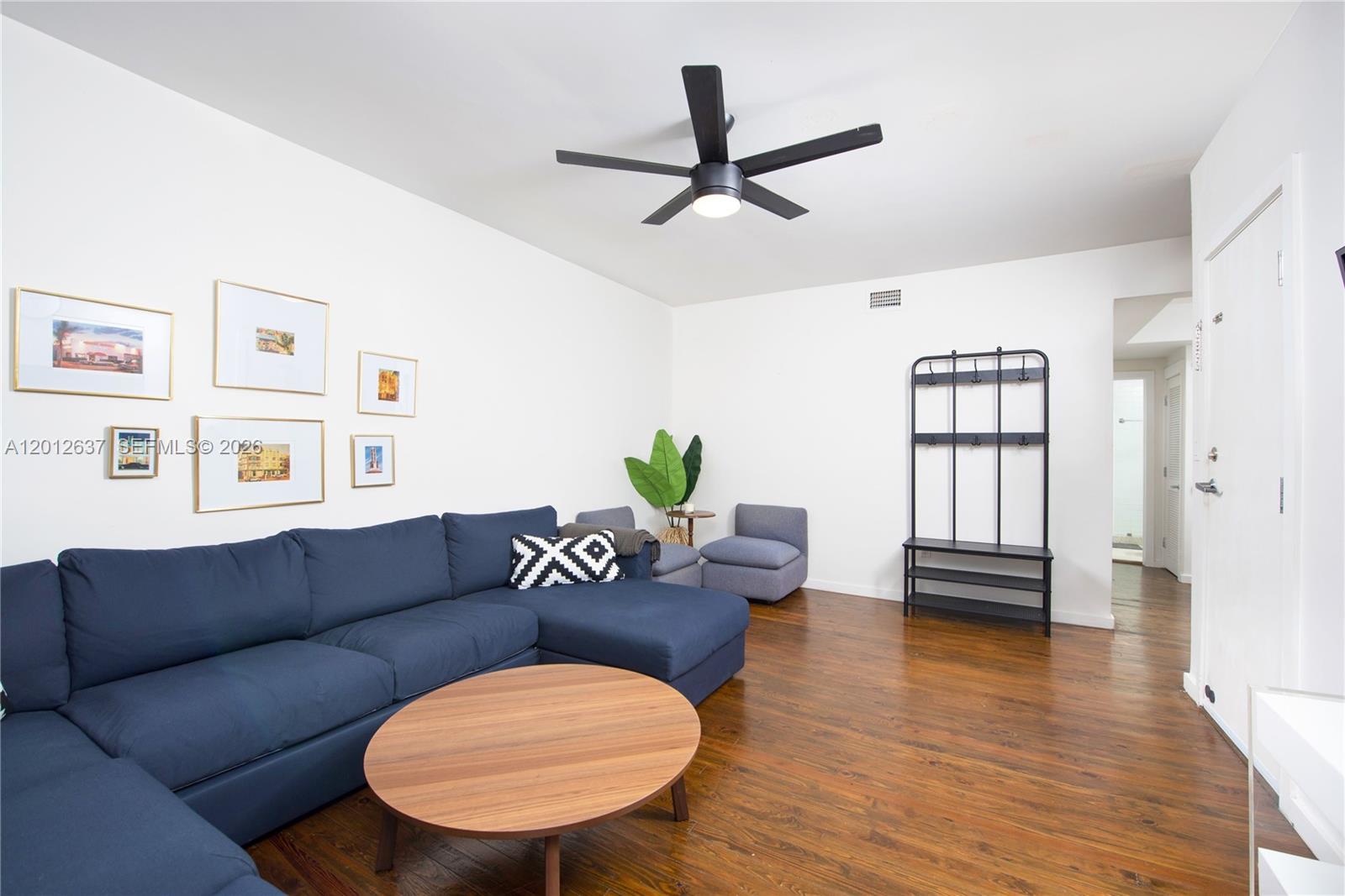 A living room features a blue sectional sofa, a round wooden table, and hardwood floors — 1616 Euclid Ave # 7, Miami Beach FL 33139, MIAMI BEACH, FL