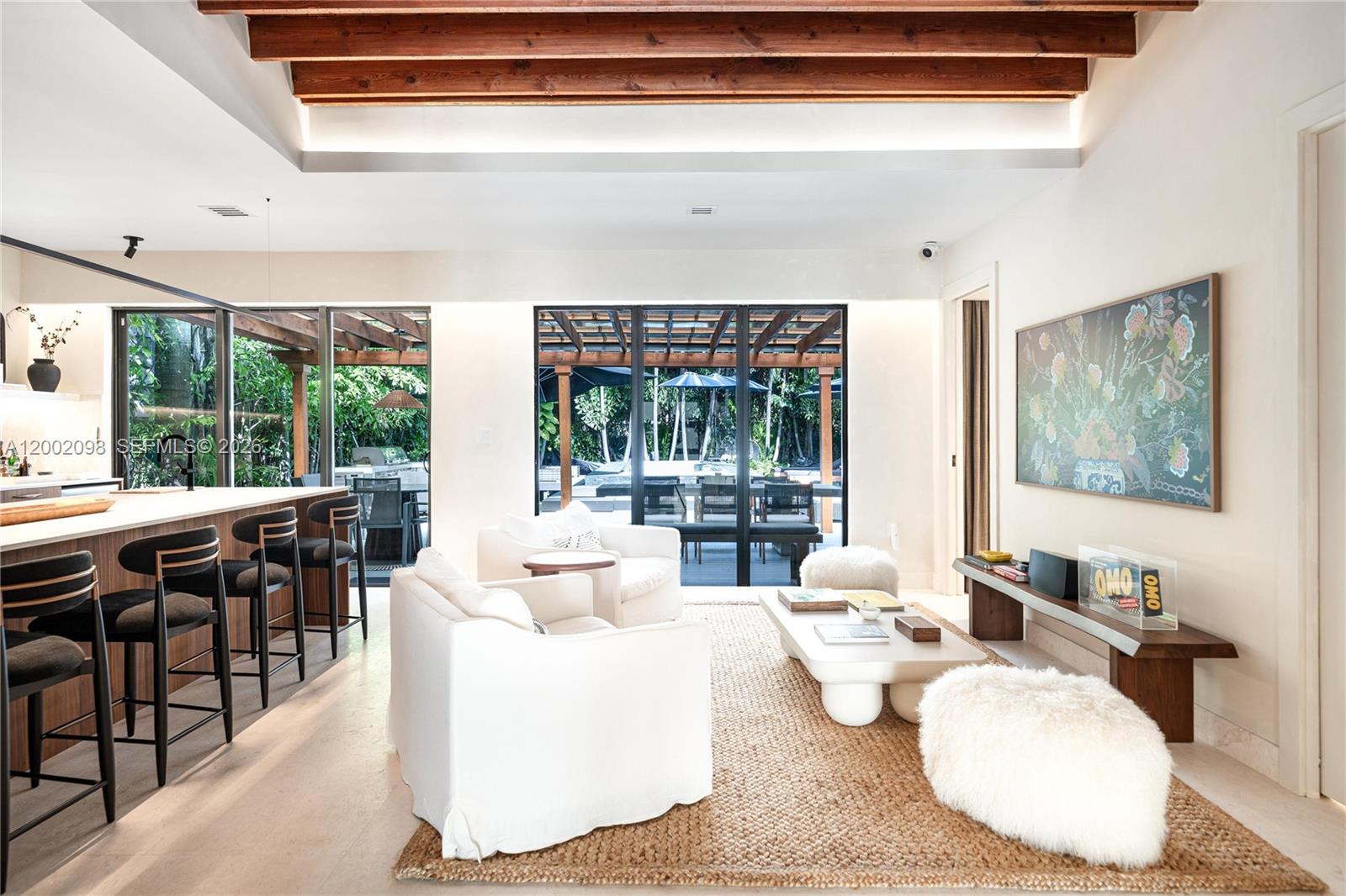 A living room with wooden ceiling beams, white furniture, and a view of a patio — 1735 Michigan Ave, Miami Beach FL 33139, MIAMI BEACH, FL
