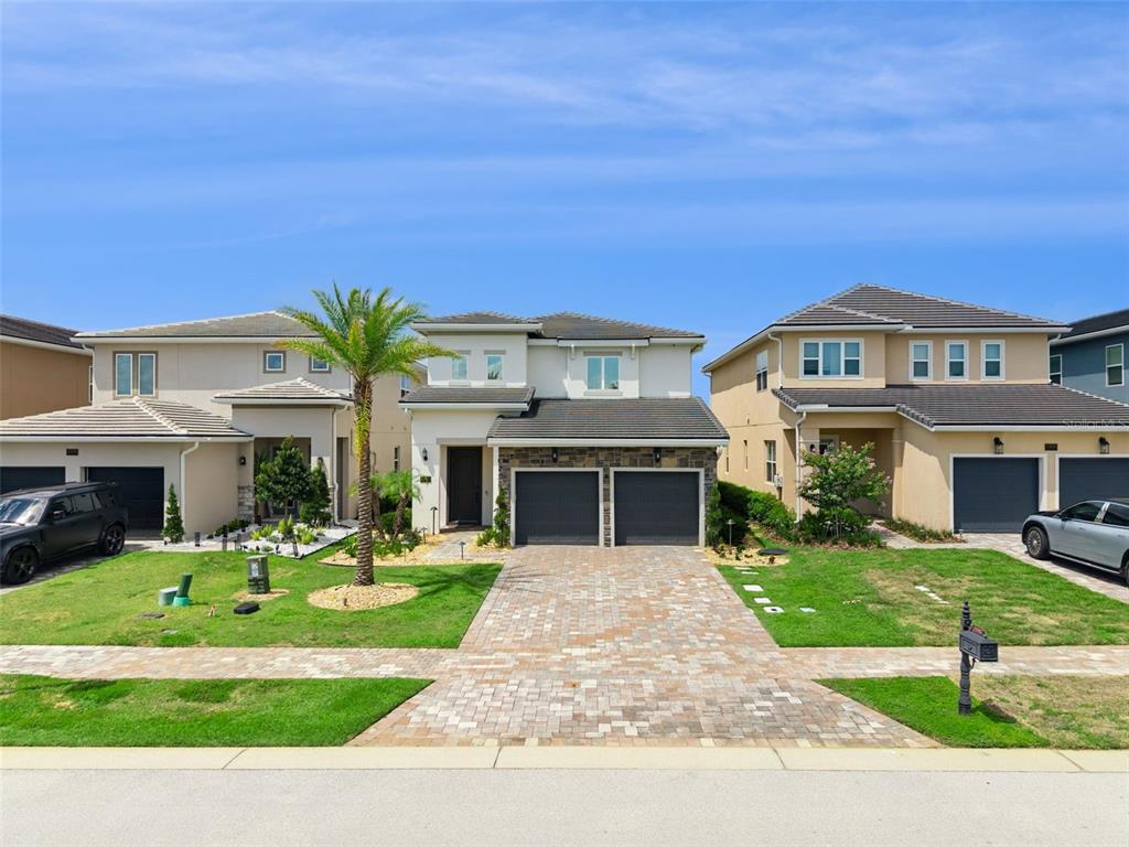 A street-level view of three modern two-story suburban houses with paved driveways and lawns — 15702 VETTA DRIVE, BELLA COLLINA, FL
