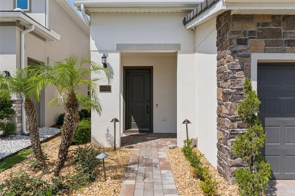 A paved walkway leads to the front entrance of a house with stone accents — 15702 VETTA DRIVE, BELLA COLLINA, FL