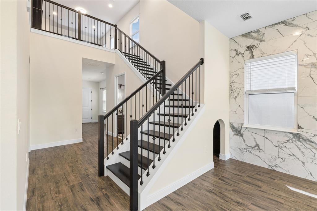 A staircase with dark wood treads and black railings stands in a room with marble-tiled walls — 15702 VETTA DRIVE, BELLA COLLINA, FL