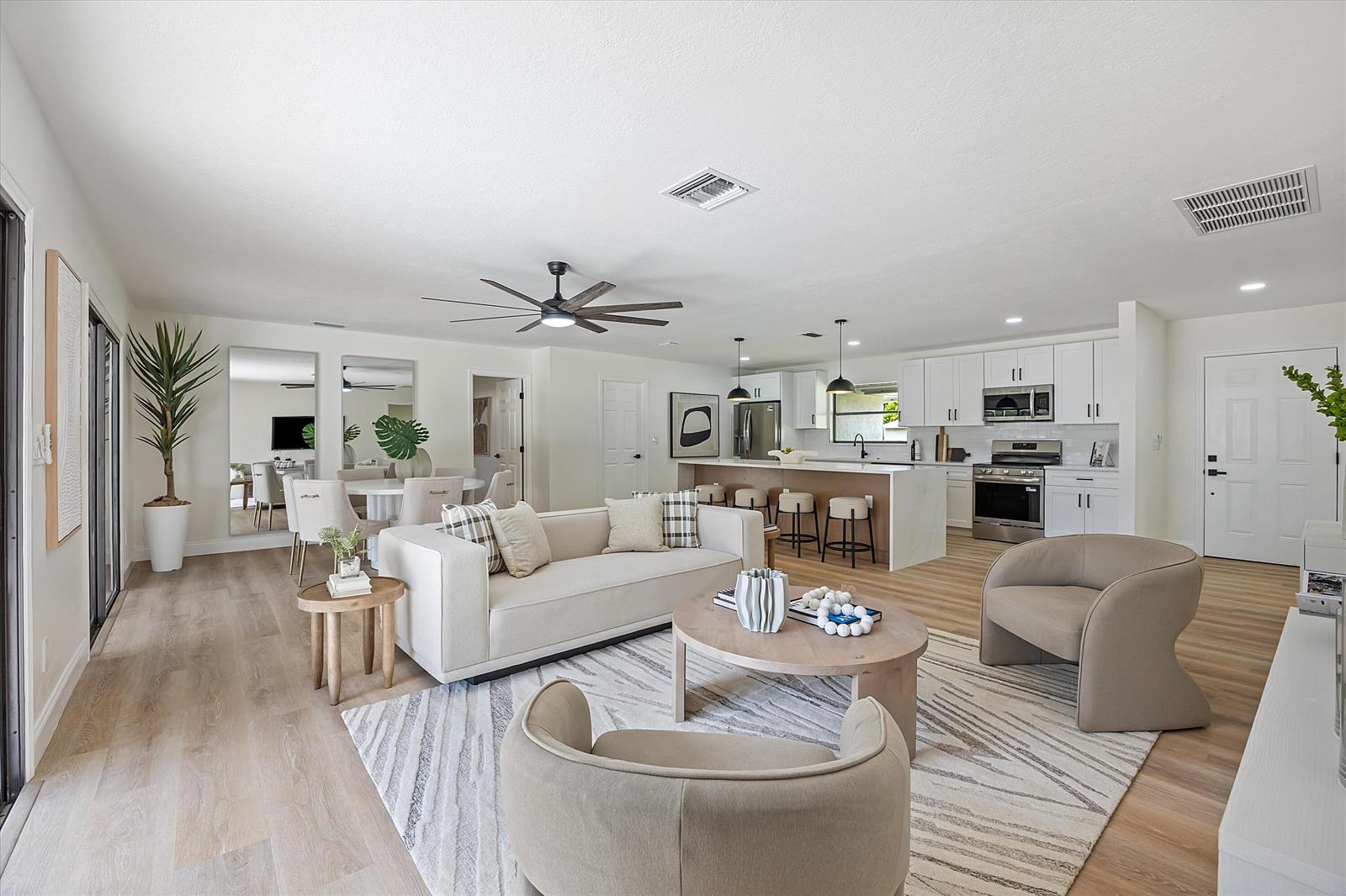 An open-concept living room and kitchen featuring light wood floors, white cabinetry, and neutral furniture — 621 NE Town Terrace, Jensen Beach FL 34957, JENSEN BEACH, FL