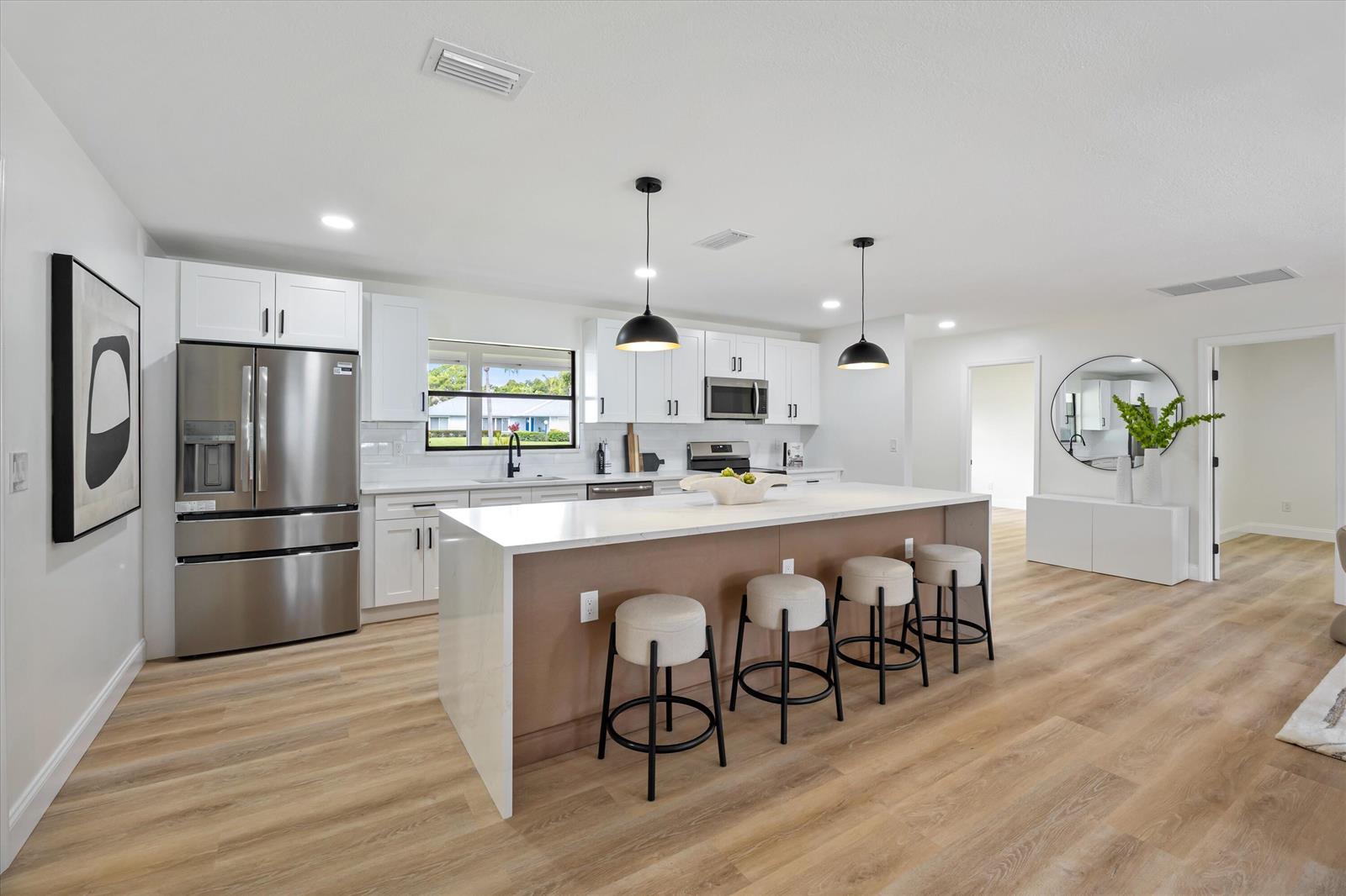 A modern kitchen features white cabinetry, stainless steel appliances, a large island, and wood flooring — 621 NE Town Terrace, Jensen Beach FL 34957, JENSEN BEACH, FL
