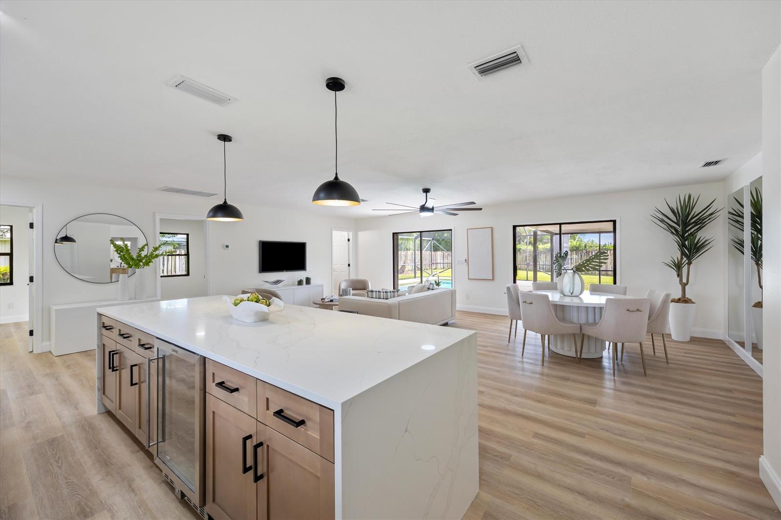 A modern kitchen island with light wood cabinets and white countertops overlooks an open living area — 621 NE Town Terrace, Jensen Beach FL 34957, JENSEN BEACH, FL