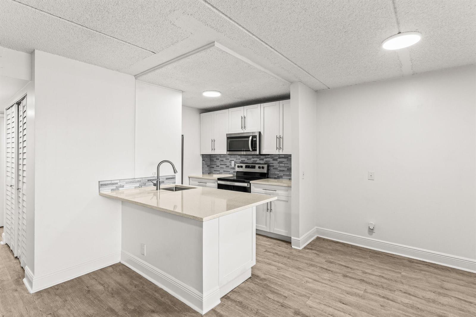 A kitchen features white cabinets, a stone countertop island, and a gray tiled backsplash — 507 Meadows Circle, Boynton Beach FL 33436, BOYNTON BEACH, FL