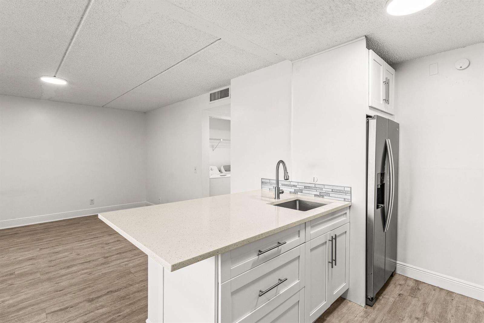 A kitchen island with a sink and quartz countertop sits in front of a refrigerator — 507 Meadows Circle, Boynton Beach FL 33436, BOYNTON BEACH, FL