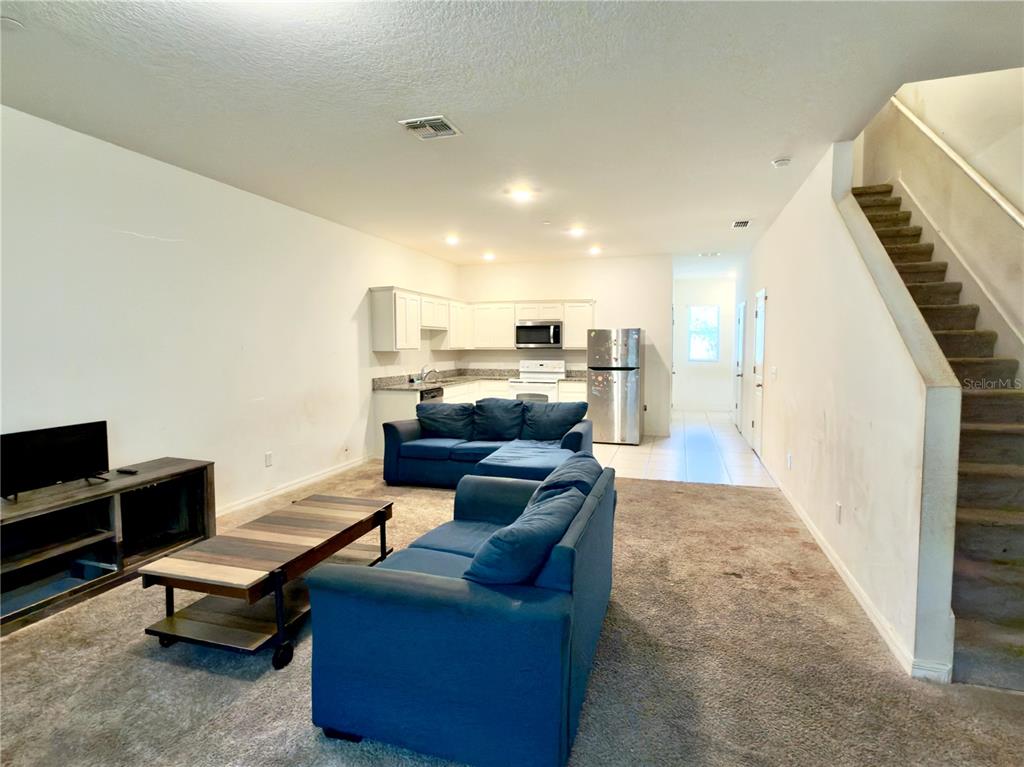 A living room with blue sofas and a coffee table opens to a kitchen area — 3139 AZOLLA STREET, ORLANDO, FL