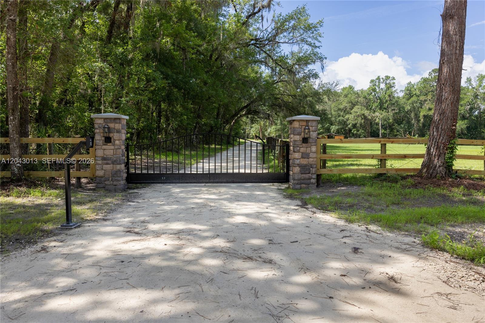 A black metal gate stands between two stone pillars at the entrance to a driveway — 14810 NW 185 ST, Ocala FL 32696, OCALA, FL