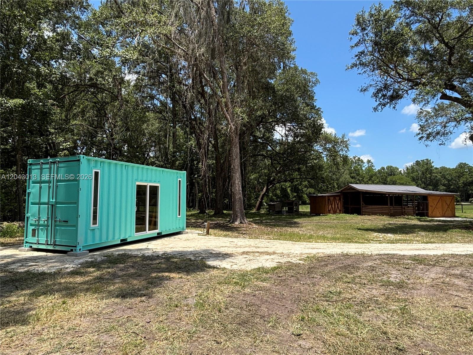 A teal shipping container home sits on a dirt lot near a wooden barn — 14810 NW 185 ST, Ocala FL 32696, OCALA, FL