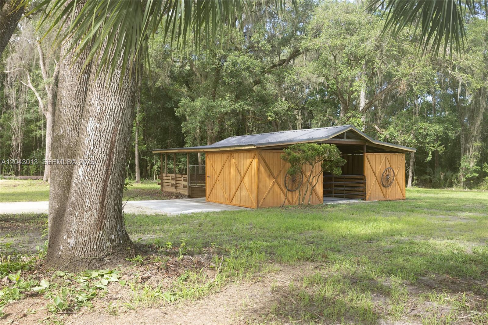 A wooden barn with a metal roof sits on a grassy lot near trees — 14810 NW 185 ST, Ocala FL 32696, OCALA, FL