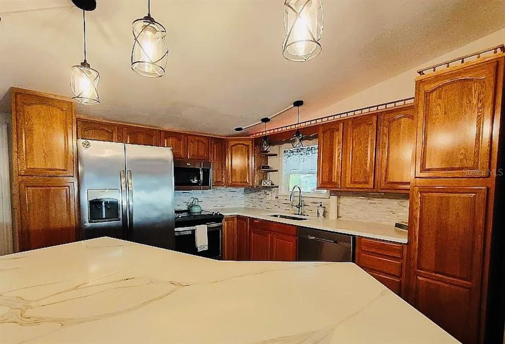A kitchen features wood cabinets, stainless steel appliances, and a large white marble-topped island — 9128 OTTER PASS, TAMPA, FL