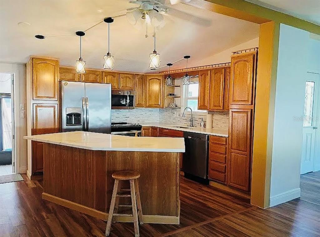 A kitchen features wood cabinets, a white countertop island, stainless steel appliances, and pendant lighting — 9128 OTTER PASS, TAMPA, FL