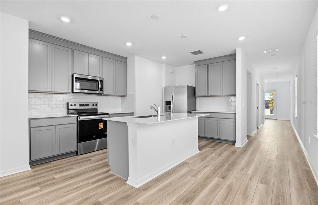 A kitchen features gray cabinets, stainless steel appliances, a white island, and light wood flooring — 1041 WENAHA COURT, ZEPHYRHILLS, FL