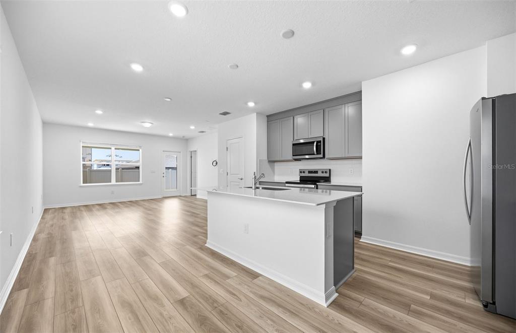 A modern kitchen features gray cabinets, white countertops, and an island, opening to a living area — 1041 WENAHA COURT, ZEPHYRHILLS, FL