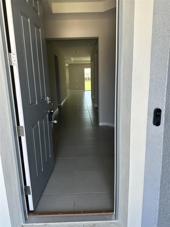 An open front door reveals a long hallway with gray tile flooring leading to a window — 4970 NW 39TH LOOP, OCALA, FL