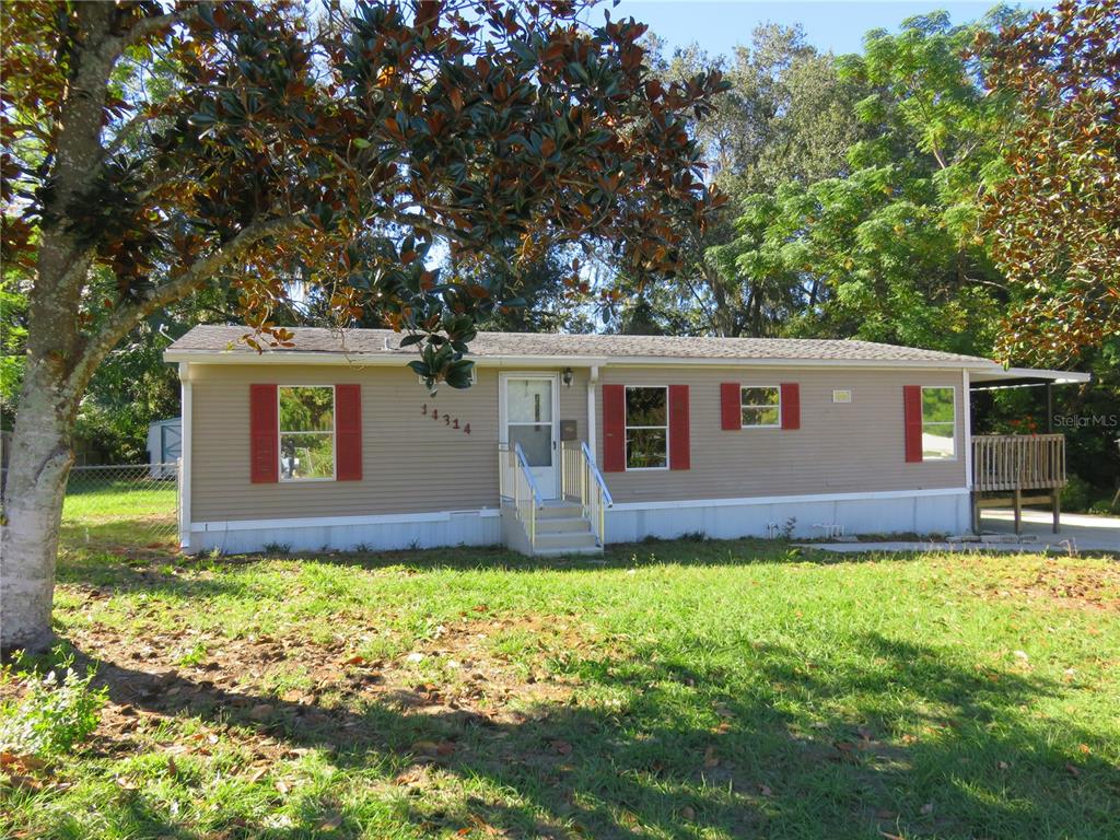 A single-story manufactured home with tan siding, red shutters, and a front porch — 14314 SE 58TH COURT, SUMMERFIELD, FL