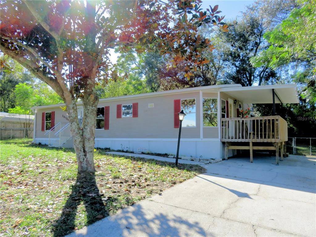 A tan mobile home with red shutters, a front deck, and a concrete driveway — 14314 SE 58TH COURT, SUMMERFIELD, FL