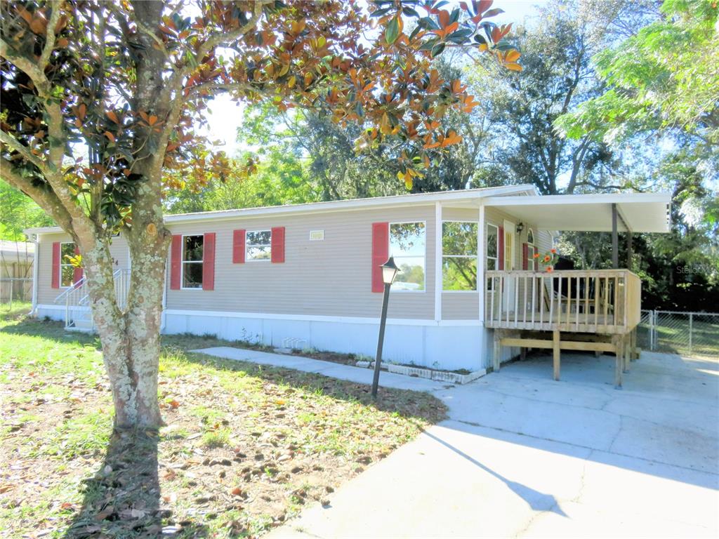 A tan mobile home with red shutters and a wooden deck sits on a lot — 14314 SE 58TH COURT, SUMMERFIELD, FL