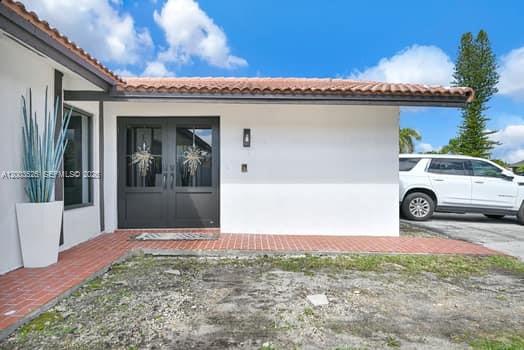A white house exterior features a dark double front door and a brick walkway — 13216 SW 45th Ln, Miami FL 33175, MIAMI, FL