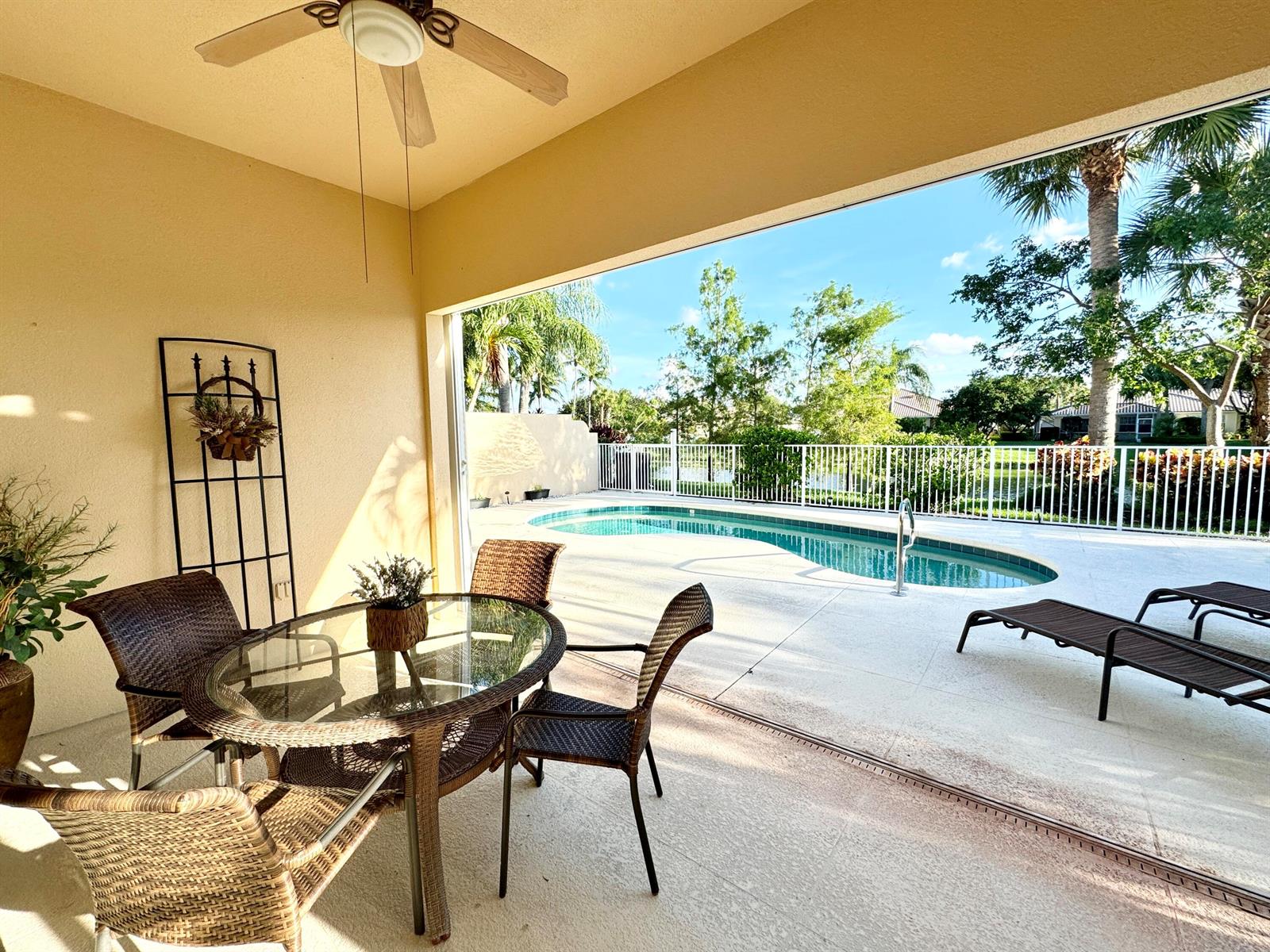 A covered patio features a glass-topped dining set overlooking a swimming pool and backyard — 8262 Dominica Place, Wellington FL 33414, WELLINGTON, FL