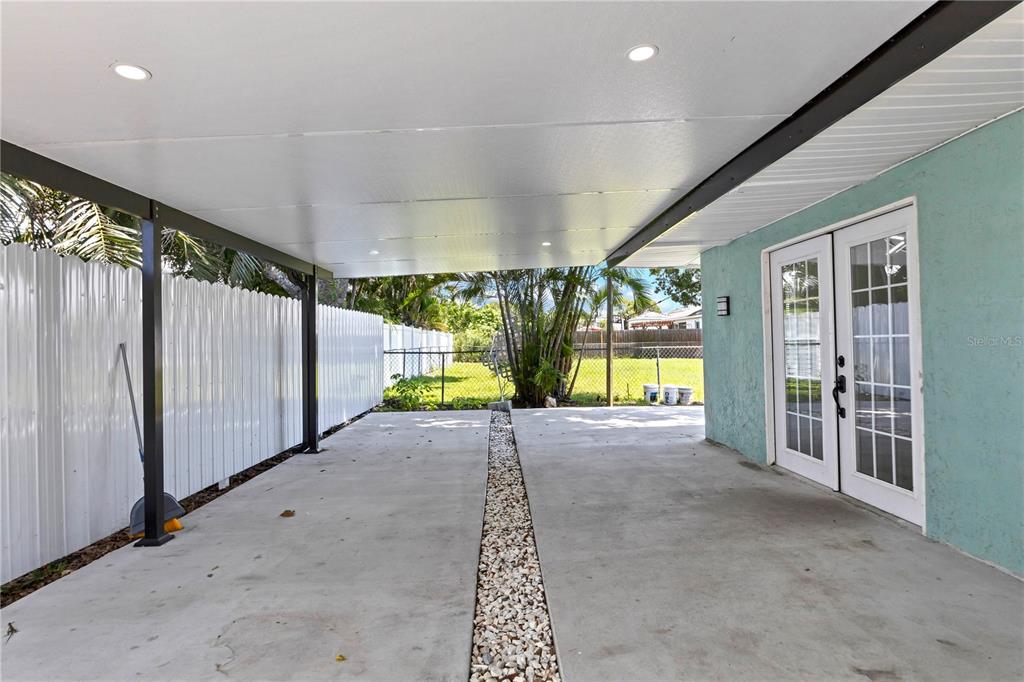 A covered concrete carport with a gravel drainage strip leads to white French doors — 2839 OLYMPIC STREET, SARASOTA, FL